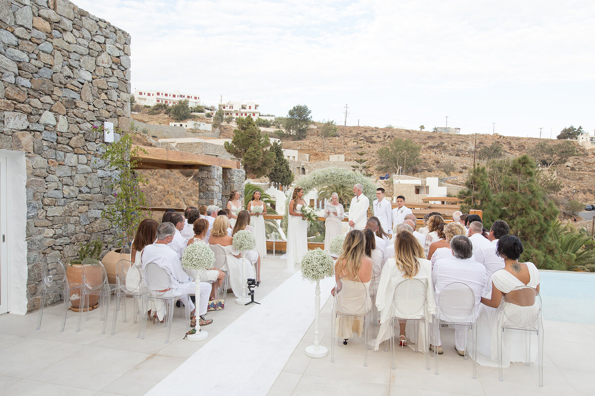 A picturesque wedding ceremony on a Mykonos Luxury villa, featuring guests in white attire gathered.