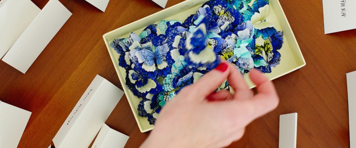 A person delicately places a card on a table beside a box of blue flowers, set for a Mykonos wedding coordination services