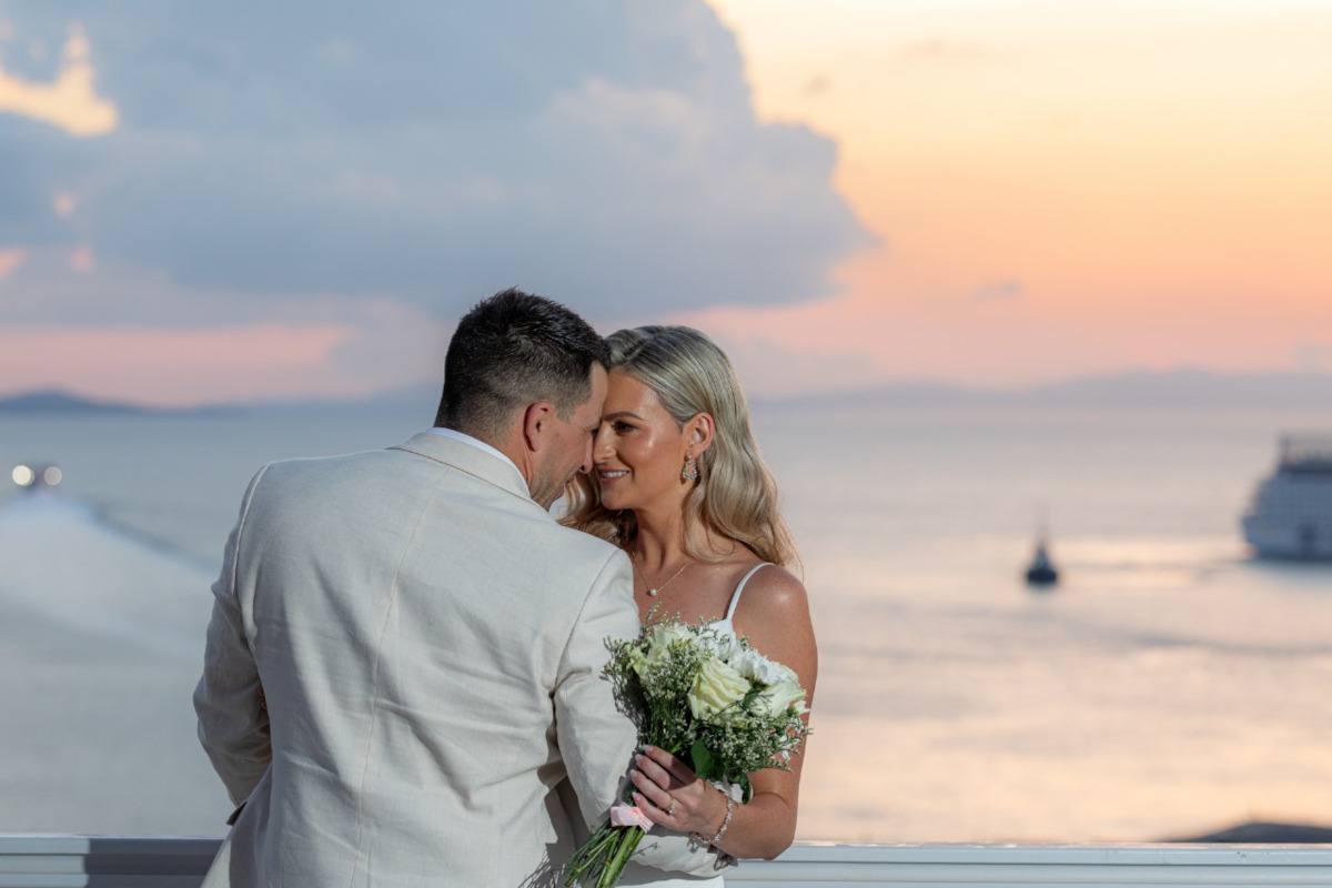 A stunning sunset in Mykonos, featuring couple holding a bridal bouquet, captured by a wedding photographer.