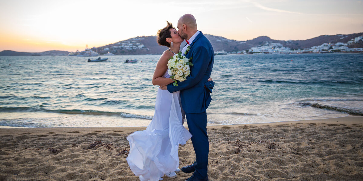 Couple kissing on the beach at sunset time after their symbolic wedding ceremony packages in mykonos